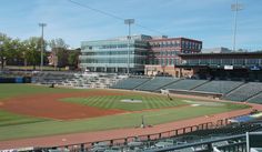 an empty baseball field in front of a large building with lots of bleachers