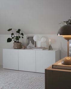 a living room with white furniture and plants on the sideboard in front of it