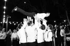 a man is thrown into the air by his groomsmen at night in front of a crowd