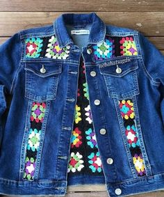 a denim jacket with colorful flowers on the front and back, sitting on top of a wooden floor