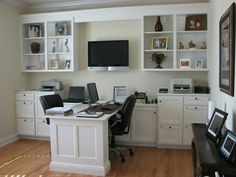 a home office with white cabinets and desks in front of a flat screen tv