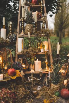 a ladder filled with candles and other items on top of a table covered in moss