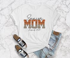 Introducing our premium T-shirt designed specifically for the proud mama of a 2025 senior basketball player! Show your support for your star athlete as they gear up for their final year on the court with this stylish and comfortable tee.   - Can be personalized with the graduation year - The word "mom" is cleverly incorporated into a basketball design, featuring trendy leopard print accents   Don't miss out on the chance to cheer on your senior basketball player in style. Upgrade your game day outfit with this must-have tee and show off your mama pride! Order yours today! Casual Custom Print T-shirt For Sports Season, Casual T-shirt With Custom Print For Sports Season, Sporty Custom Print Tops For College, Senior Basketball Mom Shirt Ideas, Varsity Style Cotton T-shirt With Custom Print, Senior Night Shirts Basketball, Basketball Senior Night Shirts, Varsity Style T-shirt With Sublimation Print For College, Senior Basketball Mom Shirts