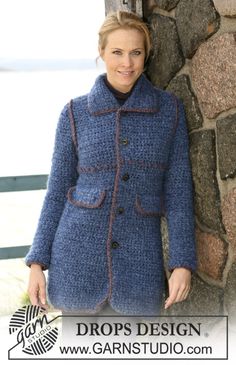 a woman standing next to a stone wall wearing a blue crocheted jacket and black turtle neck sweater