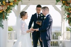 a bride and groom exchanging vows under an arch decorated with orange flowers at the end of their wedding ceremony