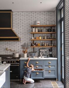 a woman kneeling on the floor in front of a stove top oven next to a counter