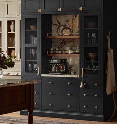 a kitchen with black cabinets and marble counter tops, gold pulls on the glass doors