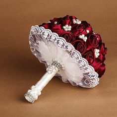 a bridal bouquet with red roses and white lace on the top is sitting next to an umbrella