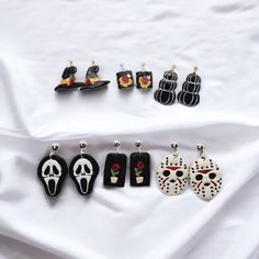 six pairs of halloween themed earrings on a white sheet with black and red decorations in the shape of skulls