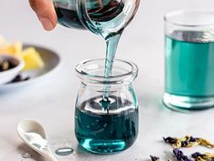 someone pouring blue liquid into a glass jar with lemon slices and lavenders in the background