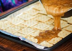 crackers being spread with caramel sauce on a baking sheet in front of a laptop