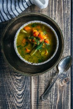 a bowl of soup with carrots and parsley in it on a wooden table