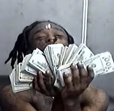 a person holding up money in front of their face while sitting on the floor with one hand over his mouth