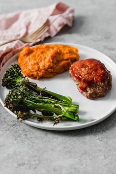 a white plate topped with meatballs, broccoli and carrots next to a fork