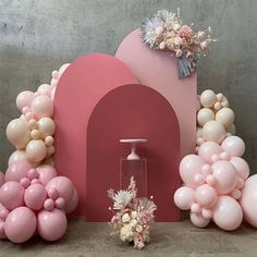 balloons, flowers and vases are arranged on the floor in front of a pink backdrop