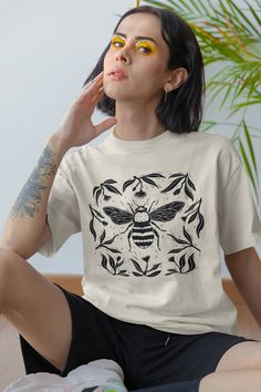 Grab this unisex shirt with a linocut aesthetic bee within botanical elements for a comfortable and stylish fashion statement. Perfect for goblincore, forestcore, fairycore and cottagecore aesthetics, this design has a mystical and artistic flare!  These unisex ultra-cotton tees are made of 100% quality cotton that is sustainably and economically sourced. The design is professionally printed using commercial-grade equipment for a long-lasting shirt that will stand the test of time, so why not treat yourself to this essential item? ------------------------------------ - 100% cotton, sustainably sourced - Heavyweight tee that holds its shape - Ribbed collar crew neck with no seam - Without side seams for a smooth fit - Shoulder-to-shoulder taping *See product pictures for sizing* ----------- Botanical Graphic Print Relaxed Fit Shirt, Botanical Style Relaxed Fit Graphic Print Shirt, Botanical Relaxed Fit Graphic Shirt, Relaxed Fit Botanical Graphic Print Shirt, Relaxed Fit Graphic Tee With Eco-friendly Ink, Botanical Graphic Print Cotton Shirt, Botanical Crew Neck Top With Graphic Print, Nature-inspired Crew Neck Tops With Screen Print, Nature-inspired Cotton Tops With Graphic Print