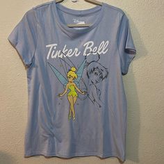 a t - shirt with tinker bell on it hanging up against a white wall