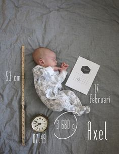 a baby laying on top of a bed next to a clock and a measuring tape