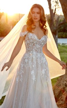 a woman in a wedding dress standing next to a tree with a veil over her head