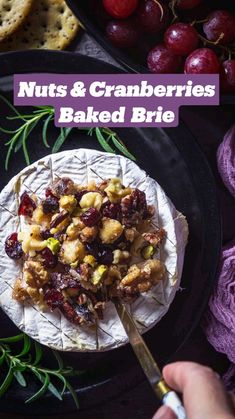 nuts and cranberries baked brie on a black plate with grapes, crackers and crackers in the background