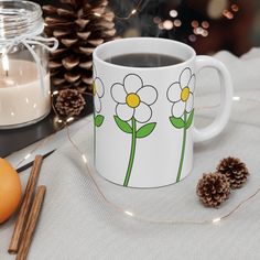 a coffee mug with flowers painted on it next to some cinnamons and pine cones