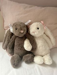 two stuffed animals sitting on top of a bed next to each other, one is brown and the other is white