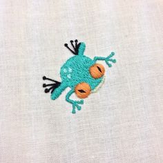 a close up of a small embroidered frog on a white fabric material with orange eyes