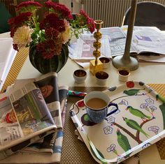 a table topped with plates and cups filled with flowers next to a vase full of flowers