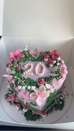 a heart shaped cake in a box with flowers and pearls on the top, surrounded by greenery