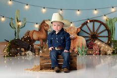 a young boy wearing a cowboy hat sitting on a crate in front of a backdrop