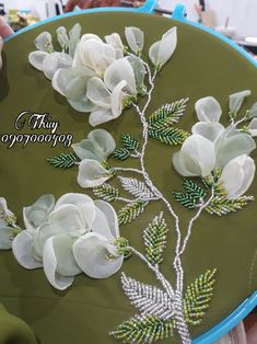 there are white flowers and green leaves on the embroidery