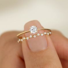 a woman's hand holding a gold ring with a diamond in the middle and two diamonds on each band