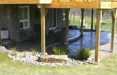 a house that has a deck and water feature in the front yard with rocks on the ground