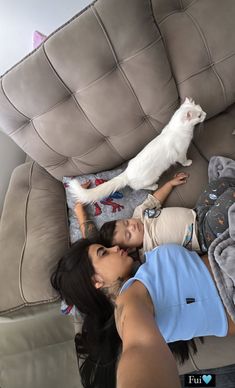 a woman laying on top of a couch next to a white cat