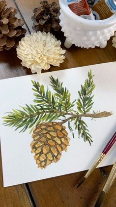 some pine cones are sitting on a table next to paintbrushes and watercolor pencils