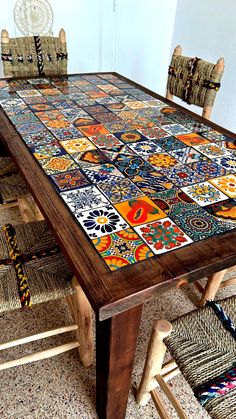 a wooden table topped with lots of colorful tile covered chairs next to a white wall