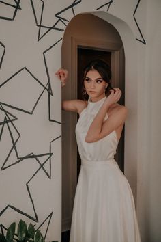 a woman in a white dress leaning against a wall with her arms behind her head