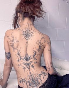 a woman with tattoos on her back sitting on a bed