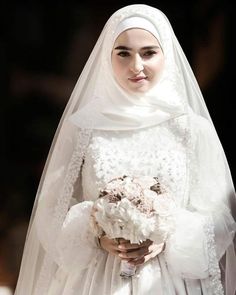 a woman in a white wedding dress holding a bouquet of flowers and wearing a veil