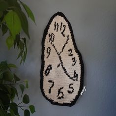 a crocheted clock is hanging on the wall next to a potted plant