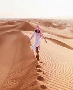 a woman in white dress walking across sand dunes