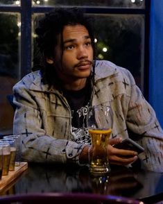 a man with dreadlocks sitting at a table in front of a glass of beer