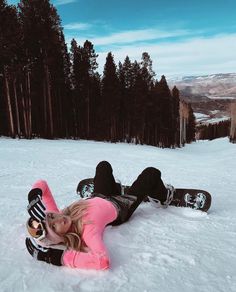 a woman laying in the snow on her stomach with a snowboard next to her