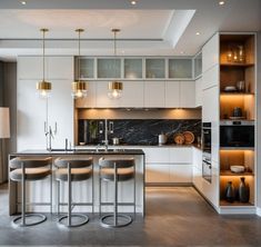 a modern kitchen with marble counter tops and stainless steel barstools, gold pendant lights, and white cabinets