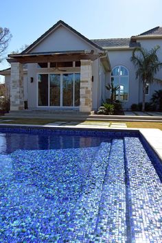 a pool in front of a house with blue tiles on the floor and side walk