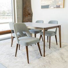 a dining room table and chairs in front of a large window with a painting on the wall