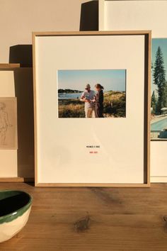 two framed photographs sitting on top of a wooden table next to a bowl and vase