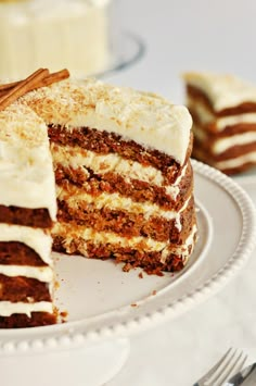 a slice of carrot cake with white frosting and cinnamon sticks on the side, sitting on a plate