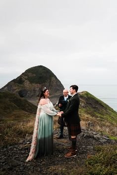 a man and woman standing next to each other on top of a hill near the ocean