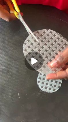 someone cutting out some paper with scissors on top of a round tableclothed surface